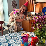 Ghost joined the competition — help win amazing prizes! woman, cat, party_hat, kitchen, table, flowers, piñata, birthday_cake, candle, window, cabinet, glasses, tattoo, smile, dress, vase, food, indoor, celebration, happy