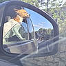 dog, car, side_mirror, window, outdoor, sunlight, trees, road, reflection, pet, animal, happy, brown, white, nature, transportation, travel, vehicle, daytime, scenery