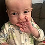 baby, child, infant, onesie, dinosaur_pattern, hand, fingers, face, eyes, couch, blanket, indoor, portrait, cute, sitting, cozy, soft_lighting, expression, young, person