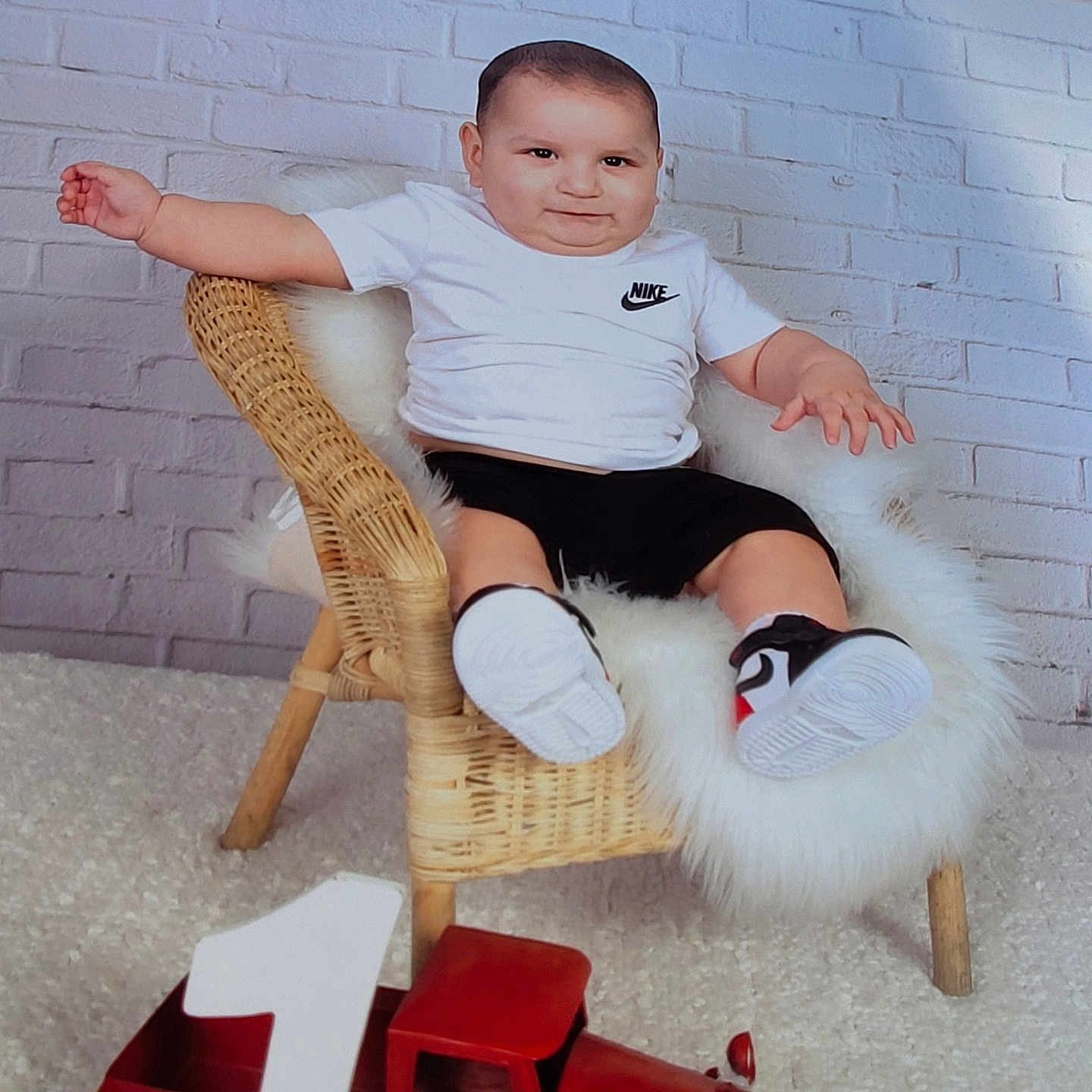Elezar is registered to the contest to win money with this photo: black_shorts, brick_wall, carpet, celebration, child, cute, first_birthday, floor, happy, indoor, nike_logo, number_one, portrait, smiling, sneakers, toddler, toy_truck, white_fur, white_shirt, wicker_chair