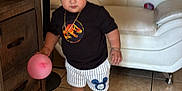 Drake joined the competition — help win amazing prizes! toddler, child, balloon, black_tshirt, dinosaur_print, striped_shorts, cartoon_emblem, black_sneakers, living_room, white_couch, wooden_furniture, tile_floor, standing, indoor, person, cute, young_child, casual_clothing, playful, bracelet