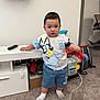 toddler, child, indoor, carpet, toy, socks, shorts, tshirt, remote_control, furniture, shoes, backpack, white_wall, cable, expression, person, standing, room, play, curious