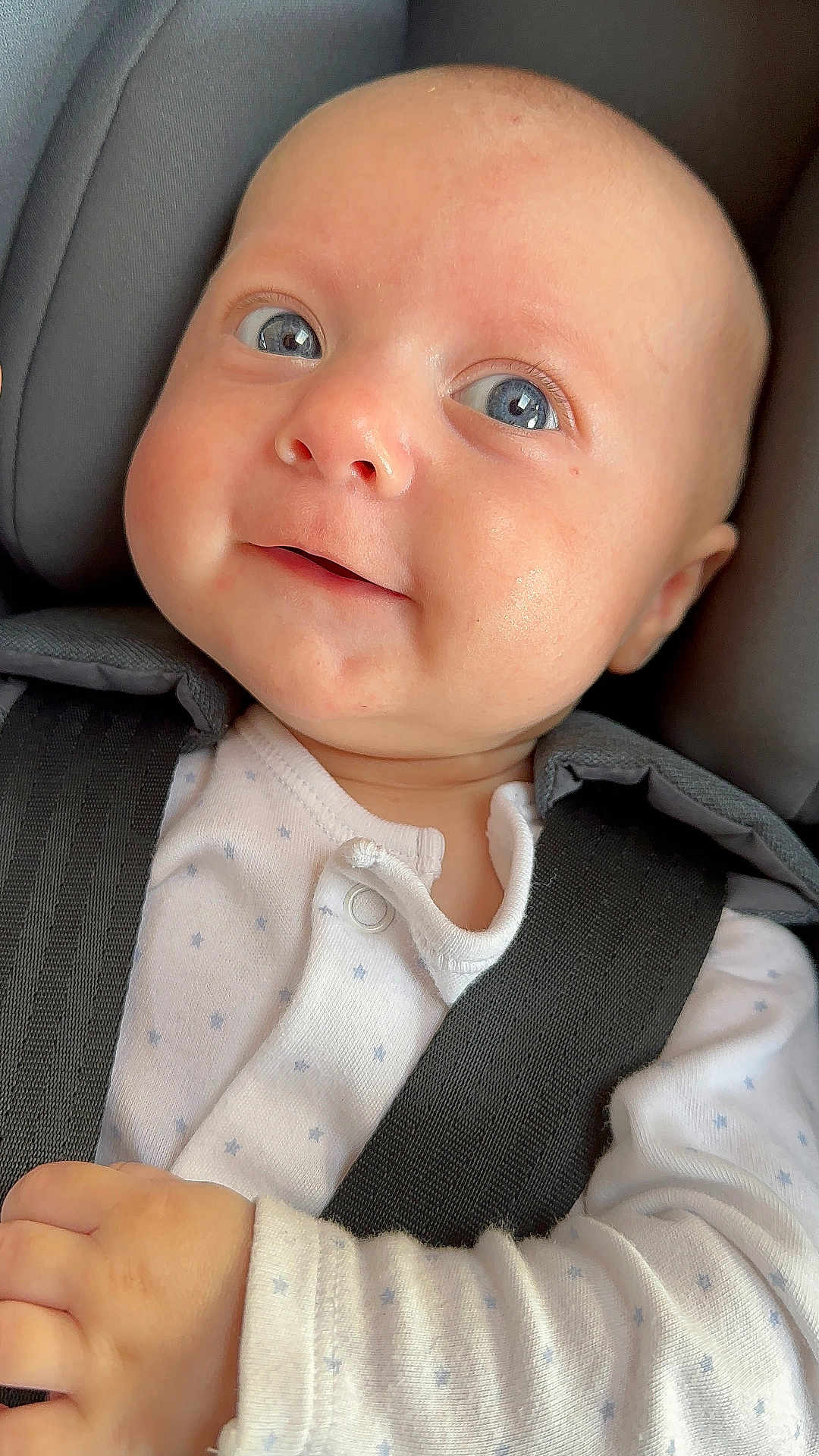 Charlie is registered to the contest to win money with this photo: baby, infant, face, blue_eyes, onesie, car_seat, seatbelt, child, cute, smile, hand, clothing, safety, portrait, closeup, skin, head, person, newborn, baby_girl
