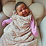 Mila is registered to the contest to win money with this photo: baby, smiling, infant, face, pink_clothing, floral_pattern, sleeping_bag, cushion, flower_shape, cozy, soft_texture, indoor, cute, child, portrait, happy, resting, comfort, warm, baby_girl