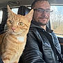 Phoenix joined the competition — help win amazing prizes! cat, orange_tabby, man, glasses, leather_jacket, car_interior, seat, window, trees, daylight, smiling, portrait, pet, animal, human, vehicle, road_trip, casual, indoor, closeup