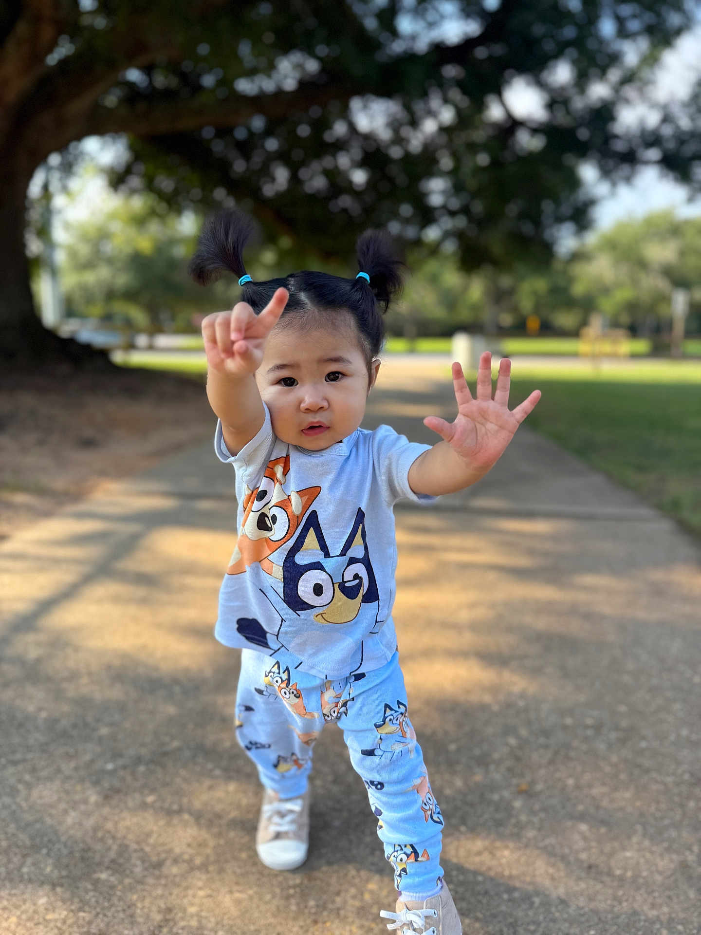 Anaia Amari joined the competition — help win amazing prizes! toddler, child, pigtails, outdoor, sunlight, cartoon_clothing, playful_pose, sidewalk, tree, greenery, shoes, casual_wear, young_child, person, cute, smiling, daylight, nature, fun, park