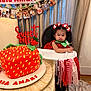 toddler, high_chair, strawberry_cake, birthday_party, cake, child, decoration, banner, ribbons, curtains, table, plate, red_dress, hair_bows, celebration, food, indoor, face, smile, person