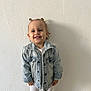 toddler, child, smiling, denim_jacket, white_leggings, standing, hair_buns, happy, indoor, wall, texture, portrait, cute, person, fashion, casual, young_child, light, face, clothing