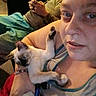 person, cat, kitten, siamese_cat, indoor, holding, relaxed, casual, sitting, phone, blue_shorts, gray_shirt, bracelet, nose_ring, furniture, couch, hand, pet, animal, portrait