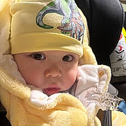 Michael is registered to the contest to win money with this photo: baby, infant, child, yellow_clothing, hat, dinosaur_print, close_up, car_seat, safety_strap, cute, soft_texture, face, eyes, indoors, warm_clothing, newborn, portrait, adorable, bundle, expression