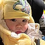 baby, infant, child, yellow_clothing, hat, dinosaur_print, close_up, car_seat, safety_strap, cute, soft_texture, face, eyes, indoors, warm_clothing, newborn, portrait, adorable, bundle, expression