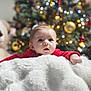 Luciana participe au concours pour gagner de l'argent avec cette photo : baby, background_blur, blanket, child, christmas_tree, cute, decorations, expression, face, festive, holiday, indoor, infant, lights, portrait, red_clothing, smiling, soft_texture, warm, winter