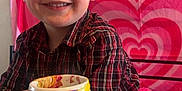 Lane is registered to the contest to win money with this photo: child, boy, smiling, plaid_shirt, mug, painted_mug, candy, bag, table, heart_pattern, background, indoor, portrait, happy, face, person, food, drinkware, colorful, casual