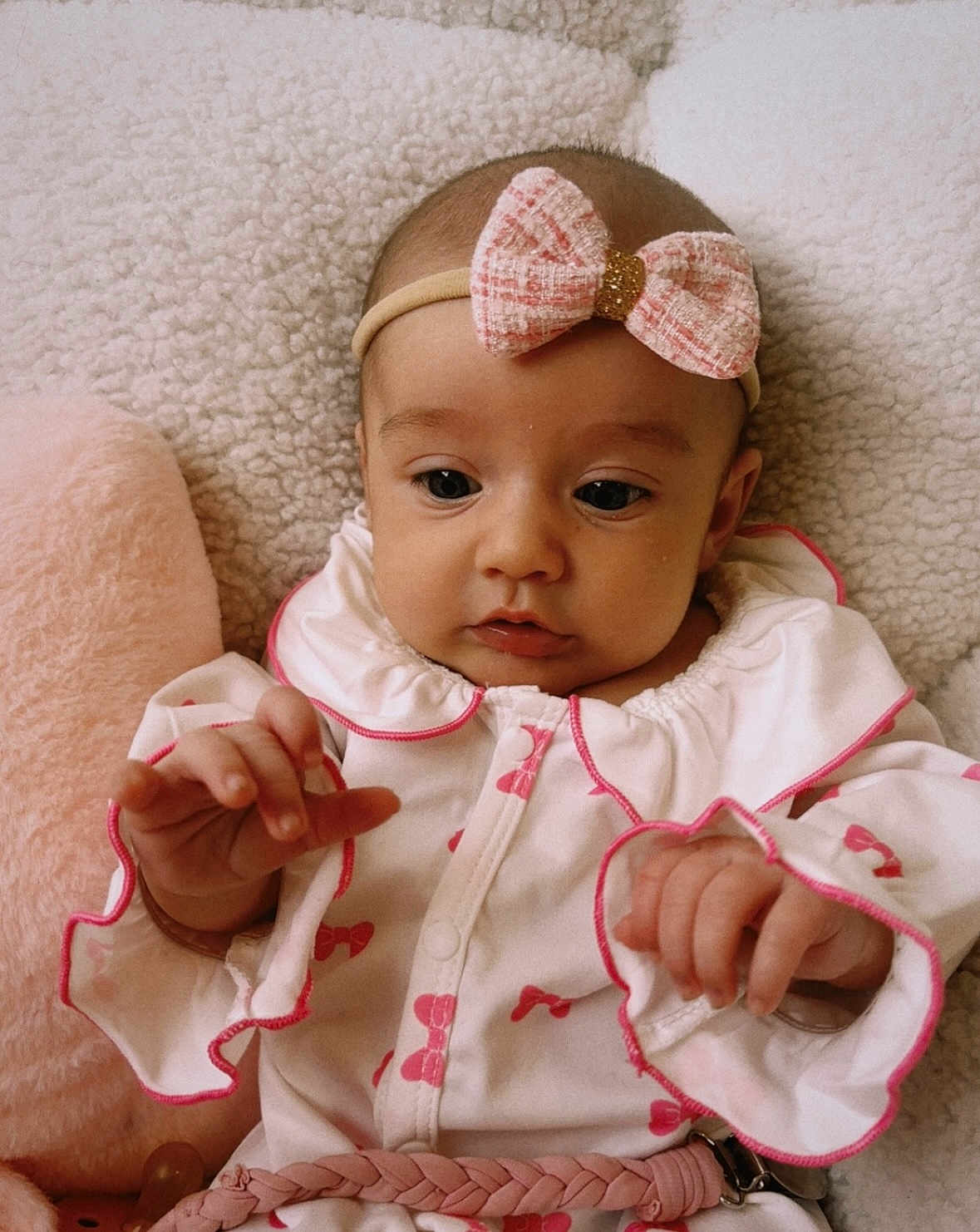 Emma is registered to the contest to win money with this photo: baby, infant, headband, pink_bow, white_clothing, blanket, hand, face, person, child, cute, soft_texture, lying_down, indoors, closeup, curious, expression, young, portrait, sleepwear