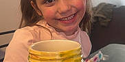 Aila joined the competition — help win amazing prizes! child, girl, smiling, portrait, indoor, painted_mug, colorful, bows, happy, table, face, long_hair, casual_clothing, art, craft, person, young, cheerful, painting_supplies, home