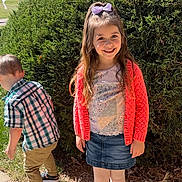 Aila joined the competition — help win amazing prizes! child, girl, boy, smile, outdoor, sunlight, greenery, bush, grass, sidewalk, clothing, plaid_shirt, skirt, leggings, sandals, hair_bow, happy, nature, daytime, playful
