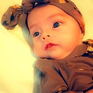 Gracie is registered to the contest to win money with this photo: baby, infant, headband, bow, clothing, cute, face, eyes, expression, lying_down, soft_light, portrait, child, newborn, skin, indoors, warm_colors, person, adorable, closeup