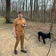 Atlas joined the competition — help win amazing prizes! boy, dog, leash, forest, trees, path, outdoor, nature, walking, boots, pants, tshirt, pet, animal, playful, brown, black_dog, leaf_litter, overcast, daytime