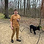 boy, dog, leash, forest, trees, path, outdoor, nature, walking, boots, pants, tshirt, pet, animal, playful, brown, black_dog, leaf_litter, overcast, daytime