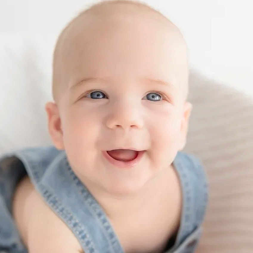 Freeman is registered to the contest to win money with this photo: baby, smiling, blue_eyes, denim_overall, happy, infant, portrait, cute, child, face, skin, head, sitting, soft_texture, light_background, innocence, expression, young, closeup, person