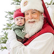 Freeman is registered to the contest to win money with this photo: baby, santa_claus, christmas_tree, holiday, festive, red_hat, beard, glasses, smiling, child, portrait, indoor, people, seasonal, celebration, costume, warm_clothing, toddler, holding, decorations