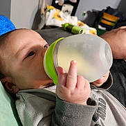 Wyatt joined the competition — help win amazing prizes! baby, bottle, hand, middle_finger, clothing, face, infant, drinking, lying_down, indoors, blanket, furniture, person, sleeve, expression, background, soft_lighting, closeup, home, relaxed