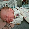 Raya is registered to the contest to win money with this photo: baby, newborn, sleeping, smiling, blanket, floral, infant, person, resting, cozy, indoor, crib, tattoo, adult, comfort, closeup, face, head, clothing, room