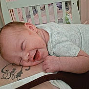 Raya joined the competition — help win amazing prizes! baby, smiling, onesie, infant, resting, tattoo, person, chest, face, hand, indoor, crib, furniture, bedroom, cozy, sleepy, cute, skin, happy, closeup