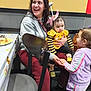 baby, bow, casual, chair, conversation, crutch, family, food_plate, hand_holding, happy, indoor, interaction, people, purple_clothing, seated, smiling, table, toddler, woman, yellow_clothing