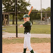 Levii joined the competition — help win amazing prizes! child, baseball, bat, sports_uniform, green_cap, green_socks, white_pants, cleats, baseball_field, dirt, home_plate, fence, outdoor, daytime, smiling, ready_to_bat, young_player, team_sport, athlete, portrait