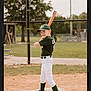 child, baseball, bat, sports_uniform, green_cap, green_socks, white_pants, cleats, baseball_field, dirt, home_plate, fence, outdoor, daytime, smiling, ready_to_bat, young_player, team_sport, athlete, portrait