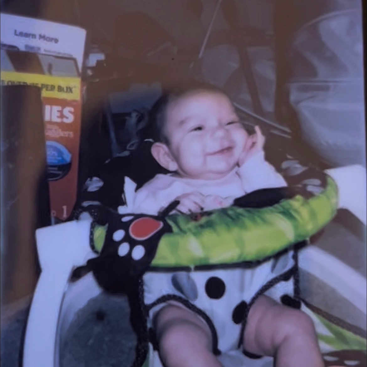 Gabriella is registered to the contest to win money with this photo: baby, baby_seat, box, cheerful, child, clothing, colorful, face, hand, happy, home, indoor, infant, legs, patterned, pink_socks, seat, smiling, snack, toy