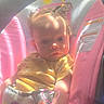 baby, child, infant, car_seat, vehicle, sitting, portrait, face, eyes, serious_expression, sunlight, indoor, travel, pink, yellow, clothing, heart_doodle, safety_label, photograph, road_trip