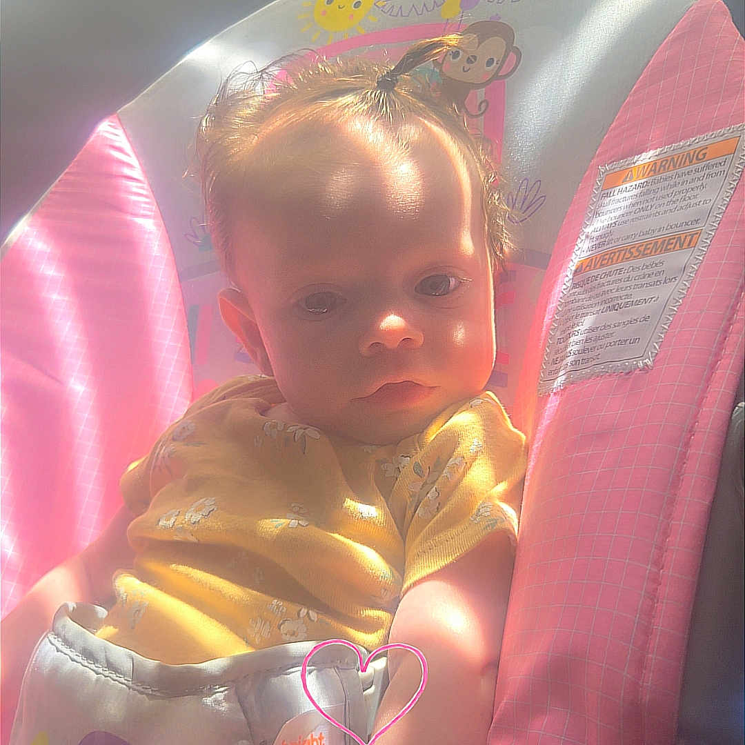 Maddelyn joined the competition — help win amazing prizes! baby, child, infant, car_seat, vehicle, sitting, portrait, face, eyes, serious_expression, sunlight, indoor, travel, pink, yellow, clothing, heart_doodle, safety_label, photograph, road_trip