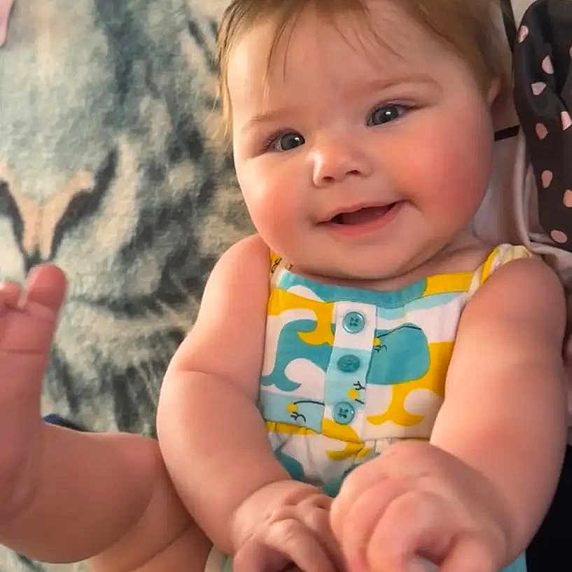 Maylee is registered to the contest to win money with this photo: baby, child, infant, smiling, happy, portrait, sitting, lying_down, onesie, colorful_clothing, barefoot, foot, hand, adult_hand, blanket, bed, indoors, close_up, family, cute