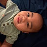 Tamasa is registered to the contest to win money with this photo: baby, child, infant, portrait, face, eyes, looking_at_camera, lying_down, blanket, clothing, long_sleeves, green_shirt, dark_background, indoor, close_up, cute, calm, head, photograph, family