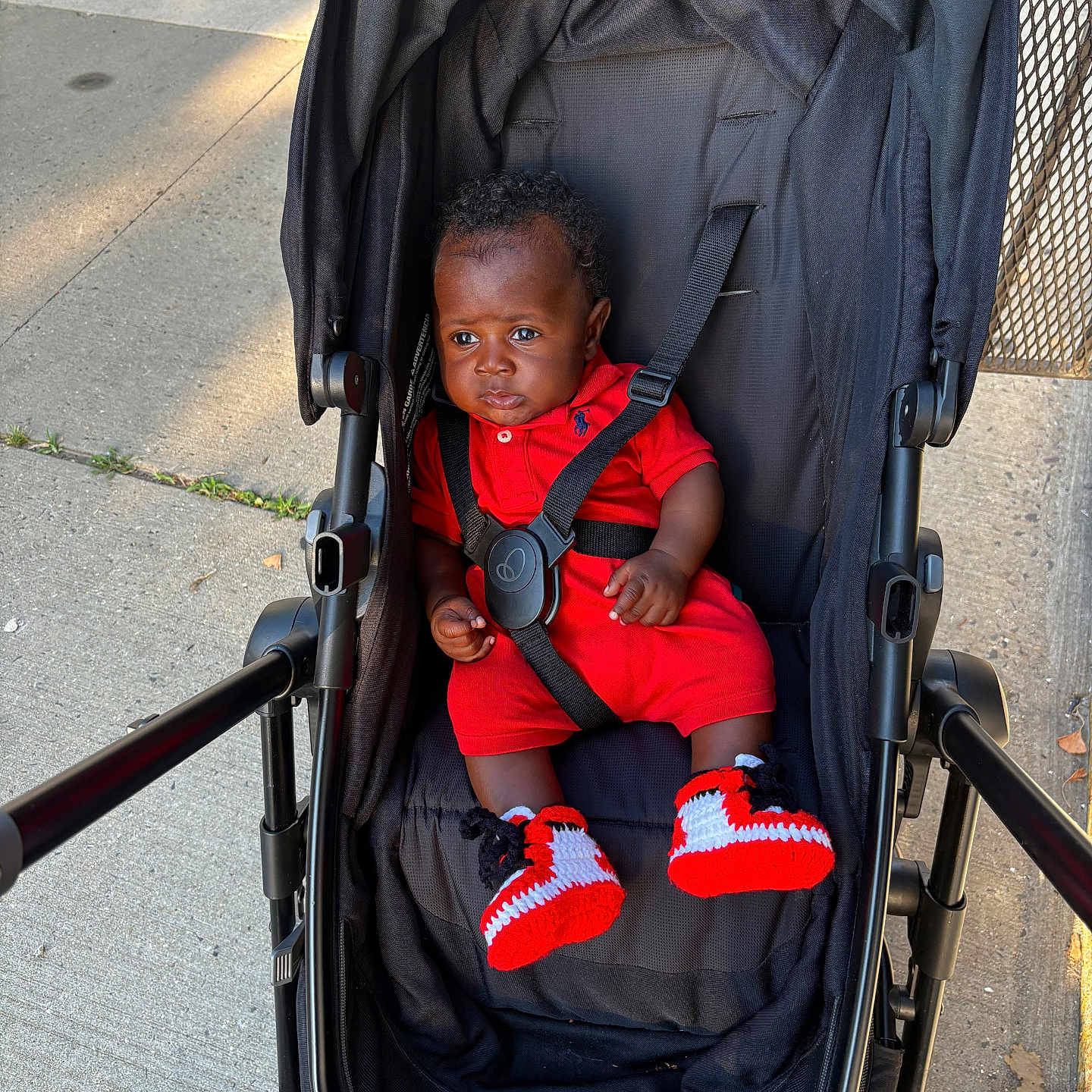 Hunter joined the competition — help win amazing prizes! baby, child, stroller, red_outfit, red_shoes, crocheted_shoes, sidewalk, outdoor, sunlight, black_stroller, curious, serious_face, urban, baby_boy, person, infant, clothing, footwear, seatbelt, casual