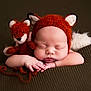 baby, sleeping, fox_hat, plush_toy, knitted, brown_blanket, cute, infant, portrait, cozy, soft_texture, child, adorable, peaceful, resting, animal_ears, newborn, hands, face, closeup