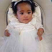 Athéna participe au concours pour gagner de l'argent avec cette photo : baby, infant, toddler, white_dress, bow_headband, curly_hair, big_eyes, necklace, bracelet, tulle_skirt, seated, stroller_seat, portrait, adorable, formal_outfit, pearl_detail, soft_lighting, closeup, smiling, baby_chair