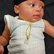 Karmello is registered to the contest to win money with this photo: baby, infant, clothing, onesie, calvin_klein, cap, gold_chain, pendant, face, skin, laying_down, looking_sideways, cute, newborn, child, fashion, accessory, portrait, indoors, black_background