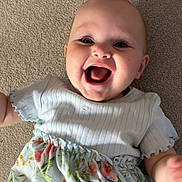 Rosalynn is registered to the contest to win money with this photo: baby, baby_dress, blue_eyes, carpet, cheerful, child, cute, floral_skirt, hand, happy, indoor, infant, person, playful, portrait, skin, sleeves, smiling, white_clothing, young