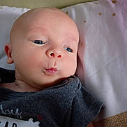Slayton joined the competition — help win amazing prizes! baby, infant, face, blue_eyes, puckered_lips, clothing, tshirt, lying_down, soft_surface, pillow, skin, head, expression, cute, child, portrait, indoors, young, person, newborn