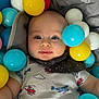 baby, child, face, smile, blue, yellow, red, white, plastic_balls, bib, onesie, airplane_print, helicopter_print, drool, happy, playful, indoor, closeup, head, person