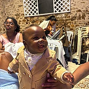 Ayden a rejoint le concours — aidez-le/la à gagner de superbes lots ! baby, child, person, smile, happy, clothing, suit, indoor, chair, table, adult, glasses, stone_wall, window, lattice, floor, hand, woman, seated, celebration