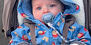 Noah is registered to the contest to win money with this photo: baby, stroller, pacifier, hooded_jacket, mittens, blanket, outdoor, pathway, greenery, cute, child, winter_clothing, blue_eyes, infant, walk, cold_weather, cozy, person, cartoon_print, beads