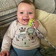 Noah joined the competition — help win amazing prizes! baby, smiling, pacifier, beads, couch, pillow, pattern, clothing, child, indoor, cute, happy, face, person, sitting, infant, toy, hand, blue_pants, long_sleeve_shirt
