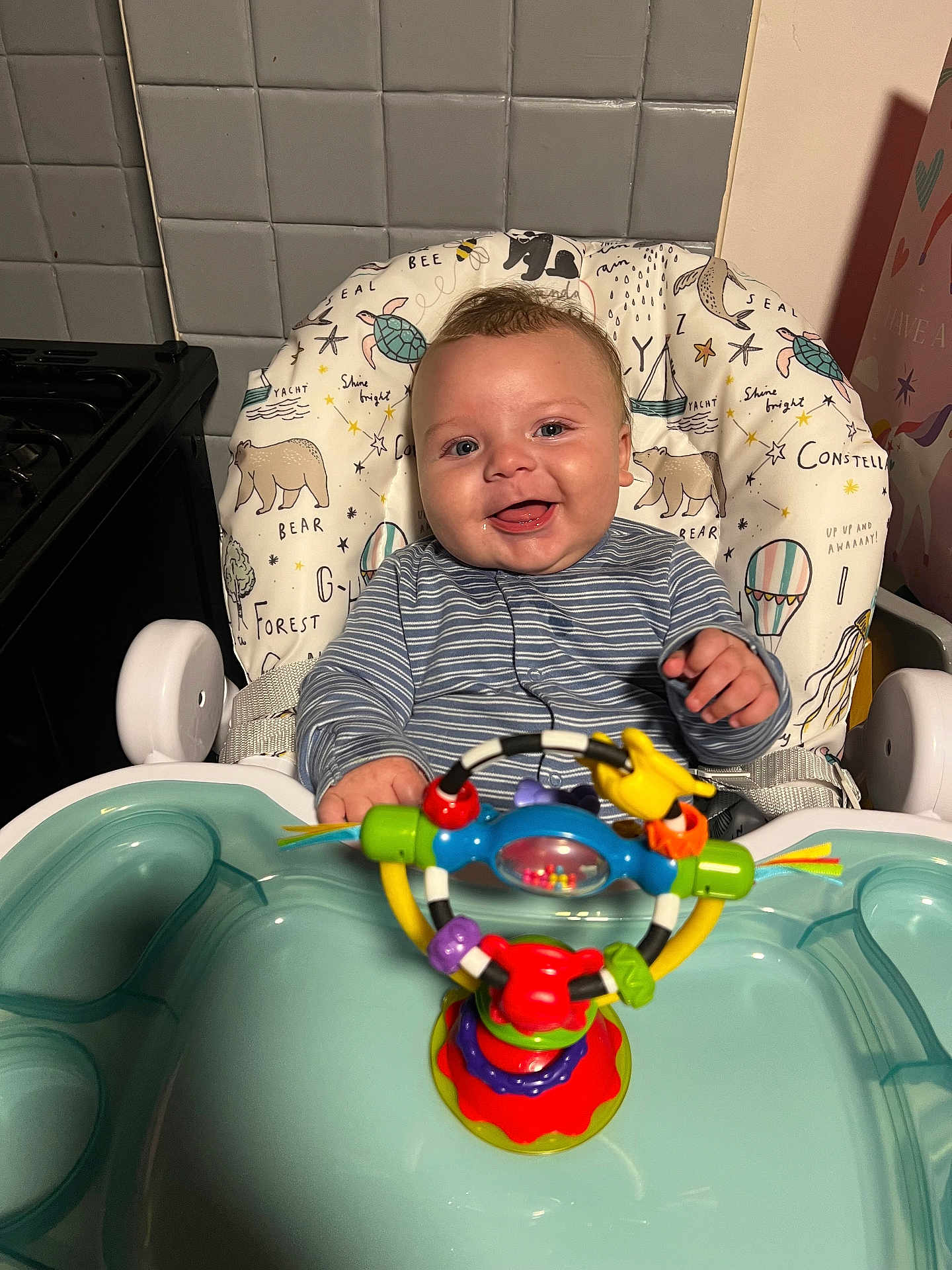 Noah joined the competition — help win amazing prizes! baby, high_chair, smile, toy, colorful, face, child, indoor, kitchen, clothing, striped_shirt, happy, seat, person, playful, cute, infant, plastic_toy, furniture, background