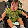 Alan is registered to the contest to win money with this photo: baby, child, stroller, green_clothing, socks, indoor, floor_tiles, curious_expression, seated, infant, young_child, hands, legs, face, head, buttoned_shirt, fabric, blanket, footwear, person