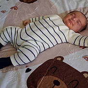 Ugo a rejoint le concours — aidez-le/la à gagner de superbes lots ! baby, infant, newborn, sleeping, smiling, face, striped_onesie, socks, blanket, bear_print, heart, rainbow, nursery_bedding, lying_down, cozy, soft_fabric, cute, portrait, bed, person