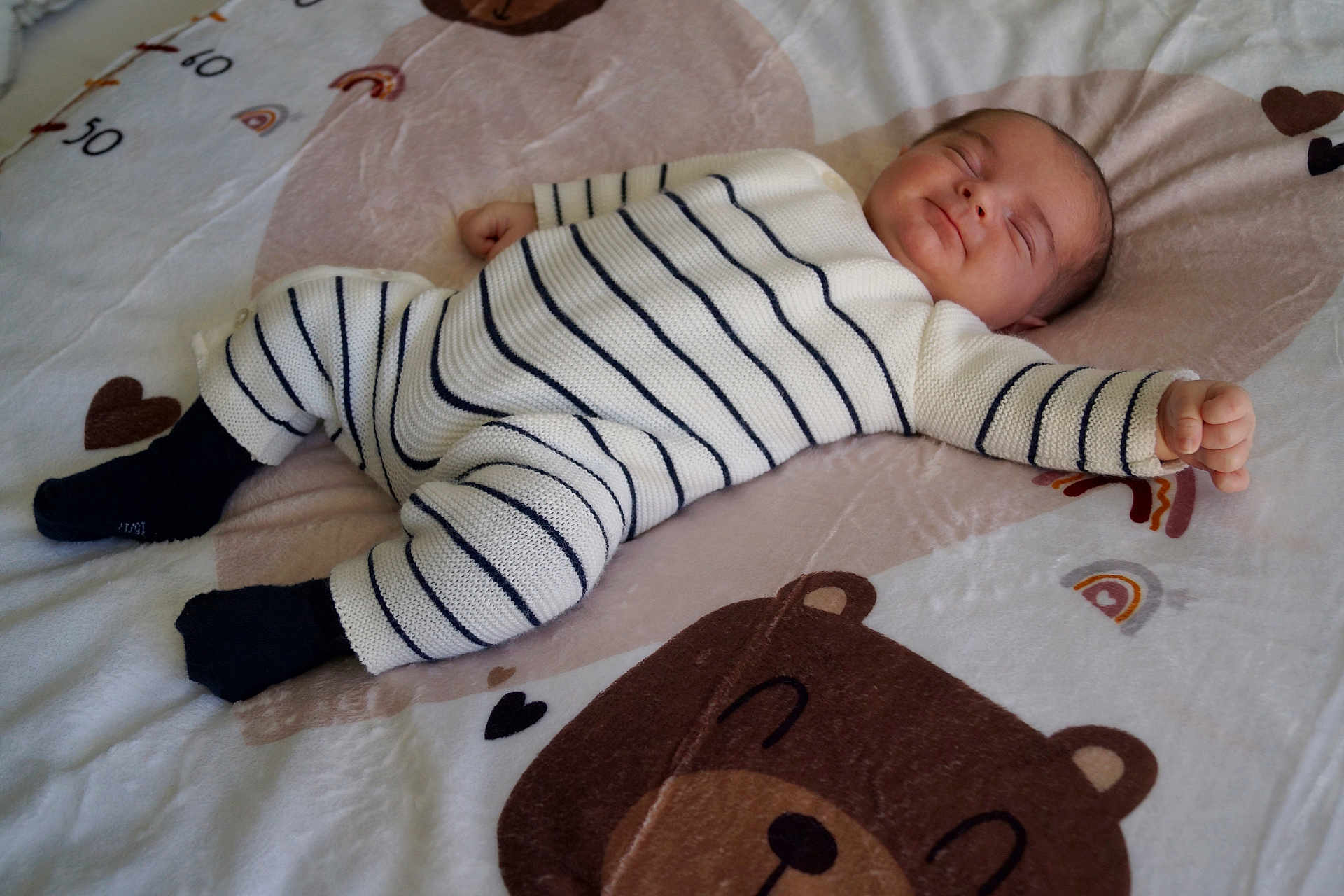 Ugo a rejoint le concours — aidez-le/la à gagner de superbes lots ! baby, infant, newborn, sleeping, smiling, face, striped_onesie, socks, blanket, bear_print, heart, rainbow, nursery_bedding, lying_down, cozy, soft_fabric, cute, portrait, bed, person